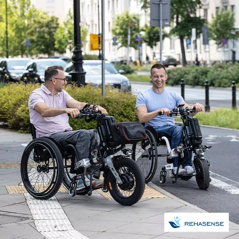 Zwei Männer im Rollstuhl benutzen das elektrische Zugsystem PAWS von Rehasense und fahren damit in der Stadt.