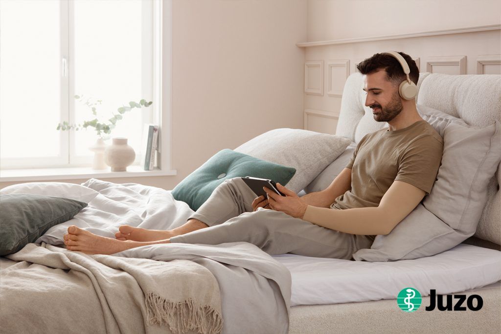 Ein Mann liegt im Bett und trägt Kompressionskleidung zur Narbentherapie und postoperativen Versorgung von Juzo.