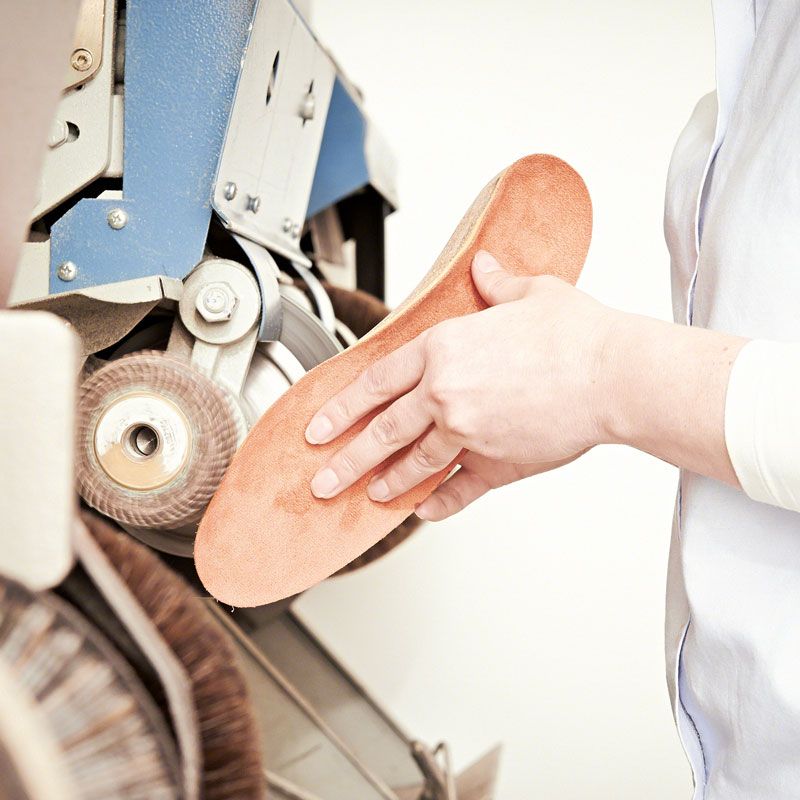 Eine Orthopädieschuhmacherin bearbeitet orthopädische Einlagen an einer Schleifmaschine.