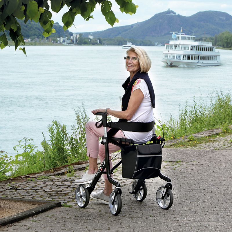 Eine Frau sitzt auf dem Xeon Rollator Carbon am See.