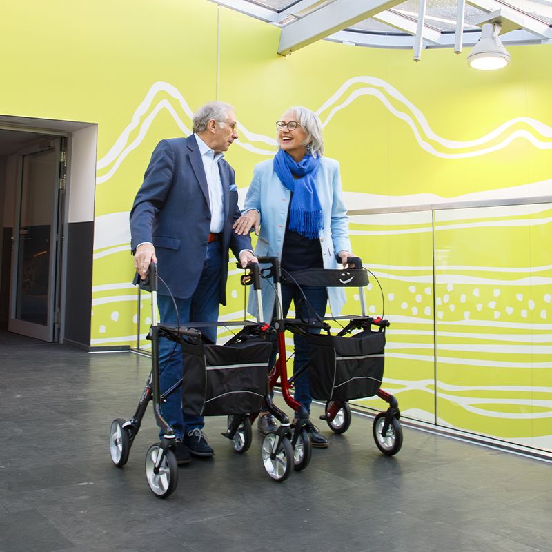 Eine Frau und ein Mann benutzen den Xeon-Rollator im Einkaufszentrum.