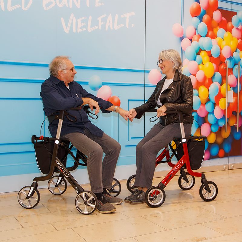 Eine Frau und ein Mann sitzen auf dem Xeon-Rollator im Einkaufszentrum.