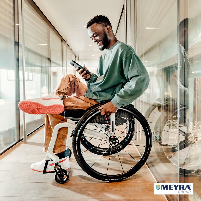 Ein Junge sitzt in einem Rollstuhl von Meyra, lacht und ist am Handy.